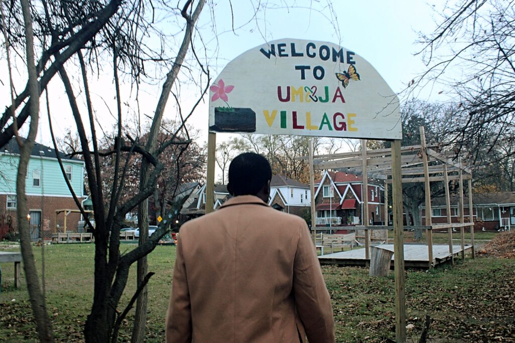 Grassy field with fallen leaves and several wooden structures, leafless trees.
