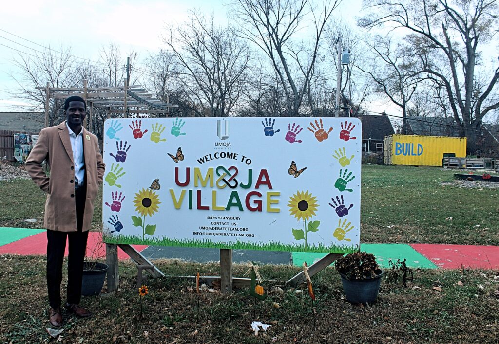 Handsome black man standing next to a sign in front of a field.